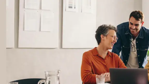 Vier Menschen unterschiedlichen Alters, unterschiedliche Hautfarben, sitzen in einem modernen Büro vor einem Laptop und sind gut gelaunt, als hätten sie gerade eine gute Lösung für ein Problem gefunden
